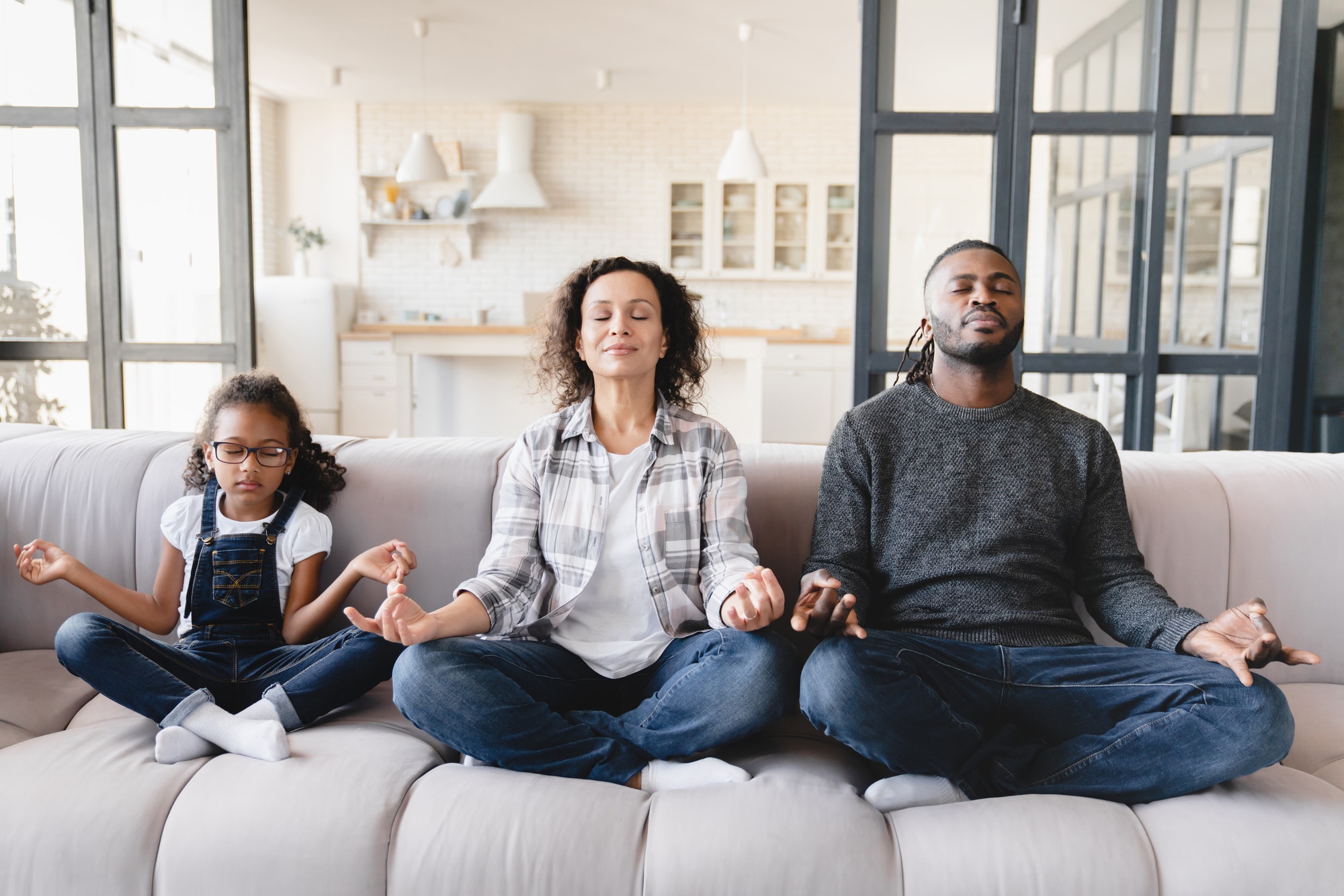 Parents with daughter meditating together at home in yoga lotus position. Stress relief. Zen-like