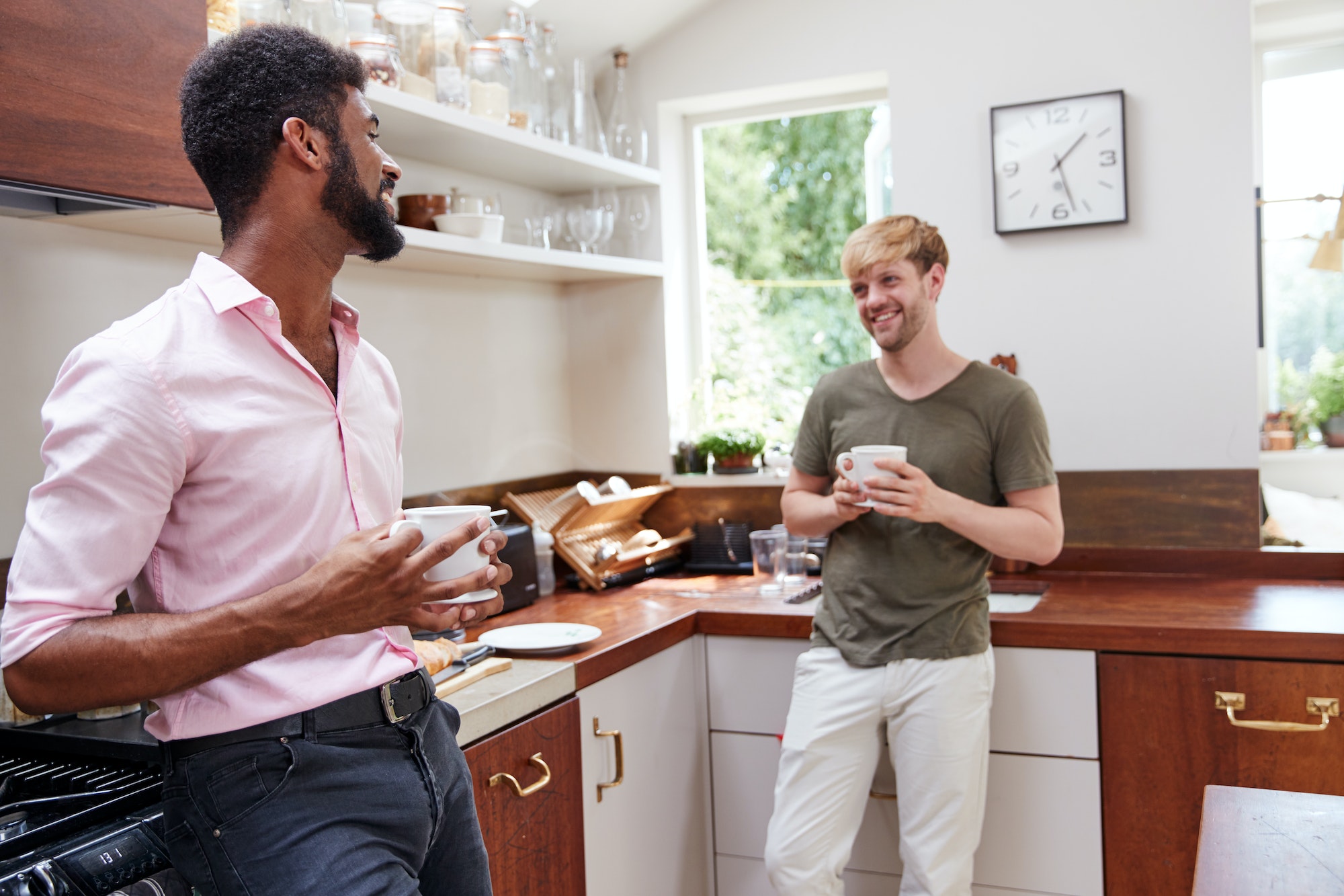 Male Same Sex Couple At Home Talking And Drinking Coffee In Kitchen Together